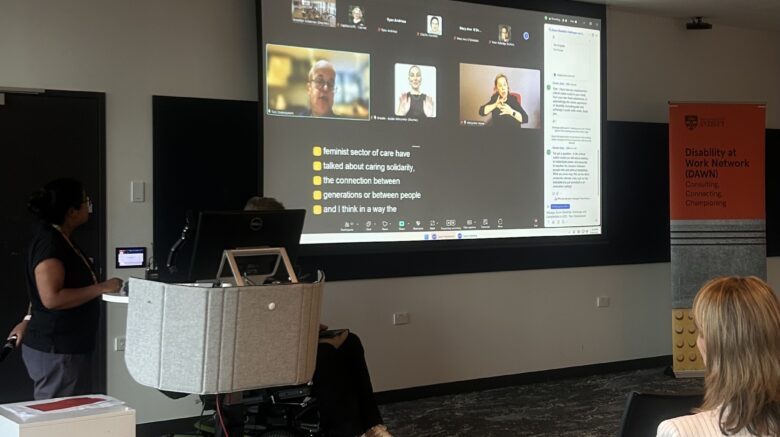 Image of the front of the room: Brooklyn and Shane next to the Zoom screen with Tom Shakespeare presenting online.